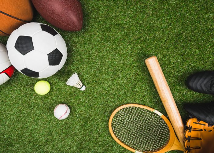 top view of various sport balls, baseball bat and glove, badminton racket on green lawn