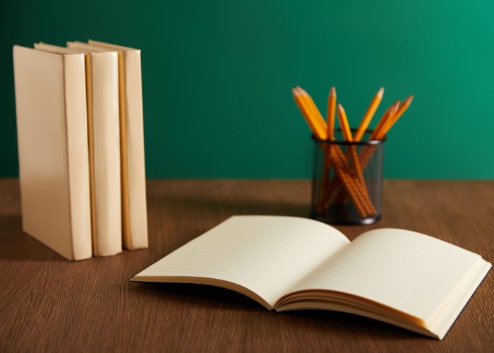 open textbook, books and pencils on wooden table